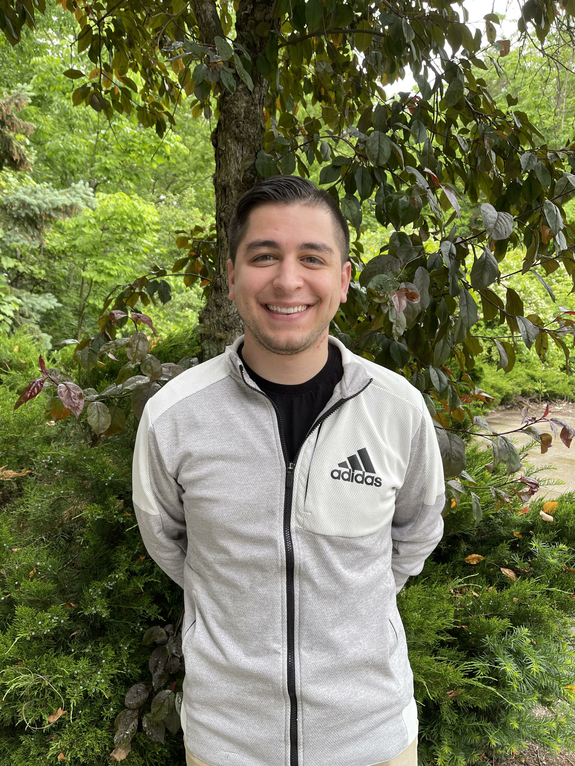 Jorge Santana smiling in front of a tree full of bright green leaves