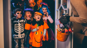 Kids in front of a door trick or treatking and homeowner giving out candy to the kids.