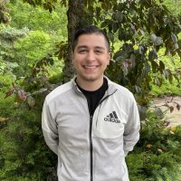 Jorge Santana smiling in front of a tree full of bright green leaves